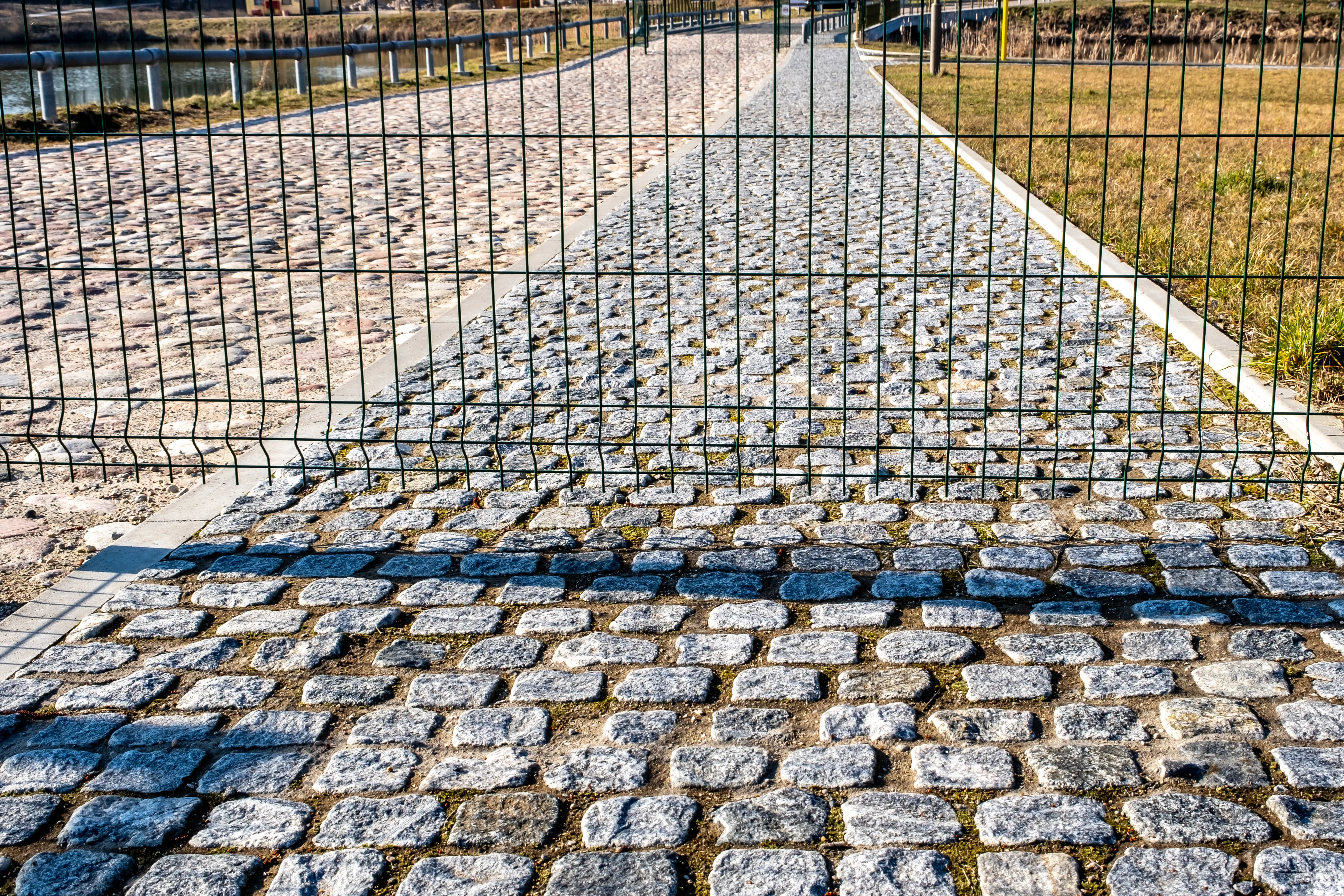 A cobblestone walkway blocked off behind a metal fence.